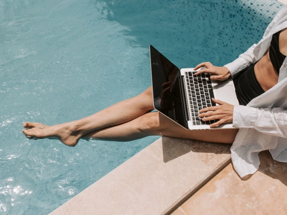 Woman with laptop next to pool.