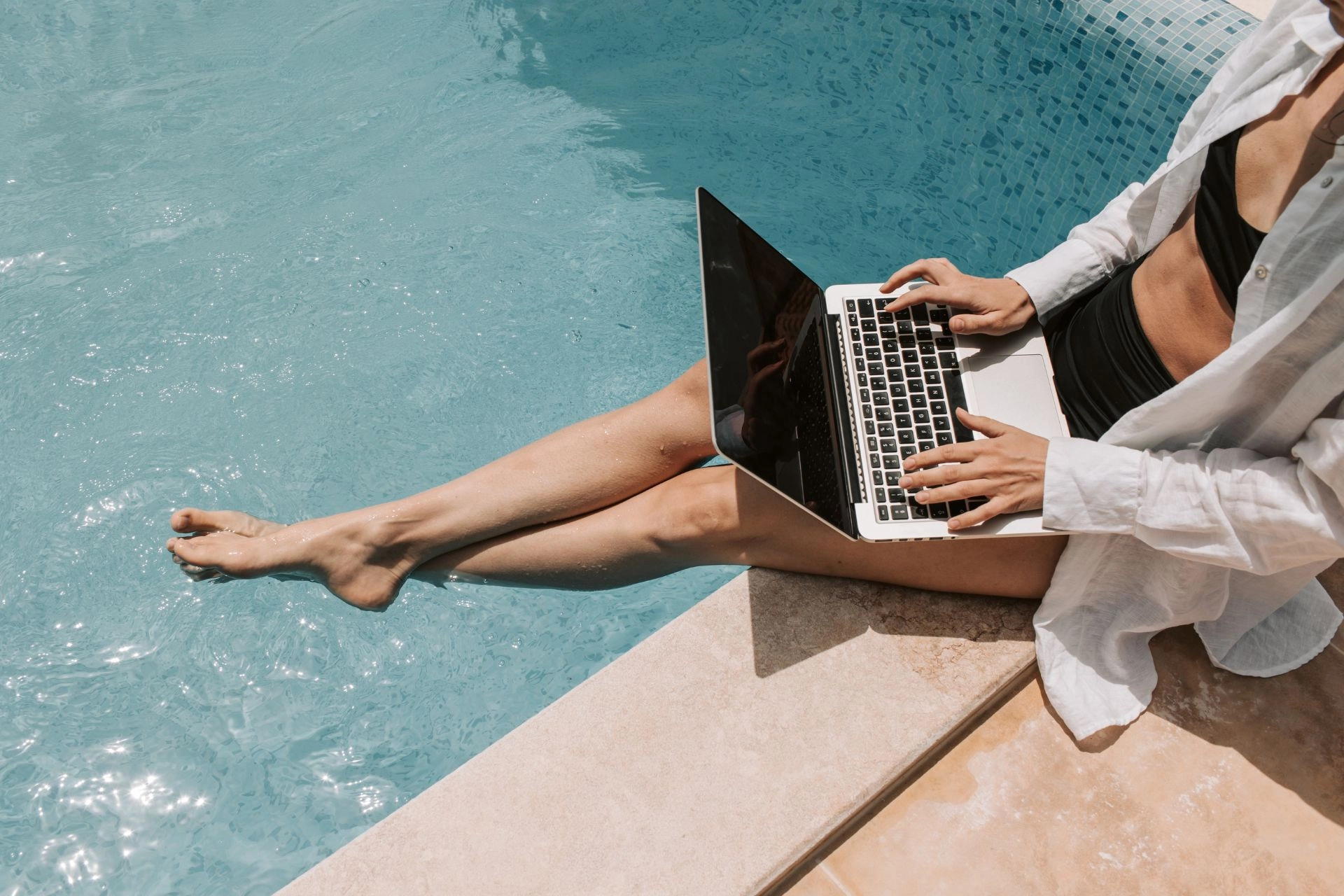 Woman with laptop next to pool.